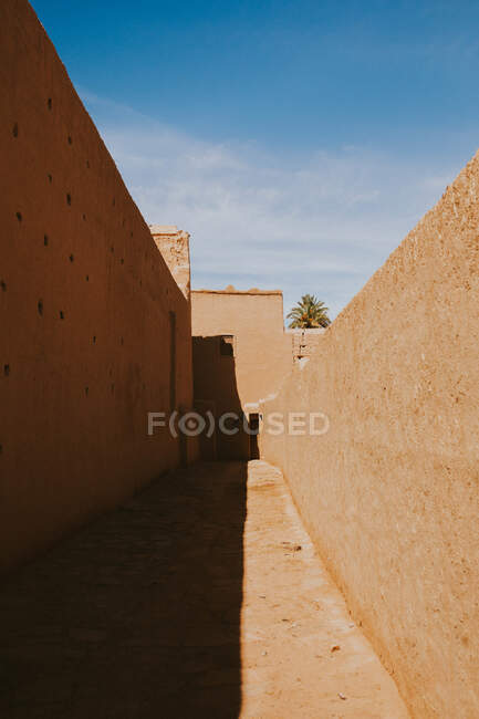 Auténtico edificio islámico con paredes llanas situado contra el cielo azul nublado en el día soleado en la calle de Marrakech, Marruecos - foto de stock