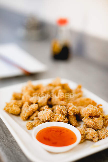 Gros morceaux de poulet rôti croustillant placés près du bol avec une sauce délicieuse sur fond blanc — Photo de stock