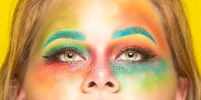 Tamaño más hembra con maquillaje de colores brillantes mirando a la cámara contra el fondo amarillo - foto de stock