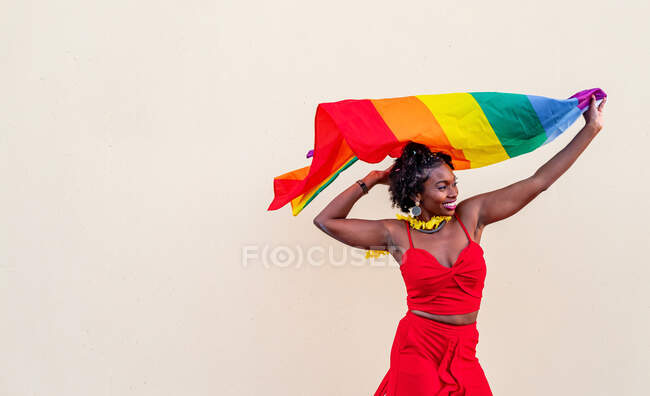 Stylish African American female in trendy clothes with colorful flag looking away during celebration — Stock Photo