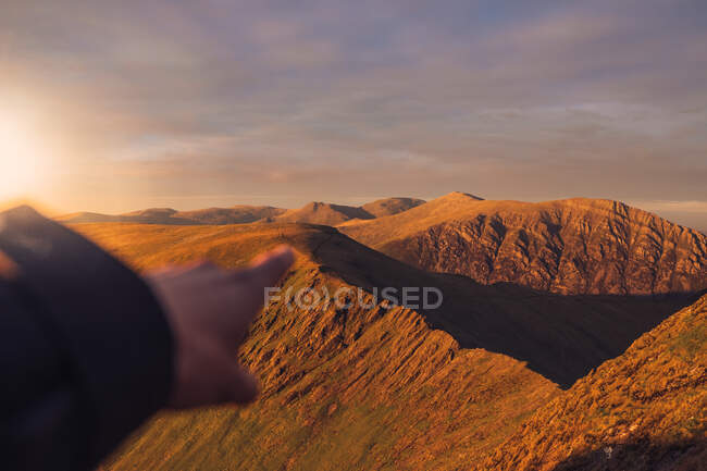 Point de vue de la culture randonneur méconnaissable pointant loin dans les hautes terres sous le ciel couchant pendant la randonnée au Pays de Galles — Photo de stock