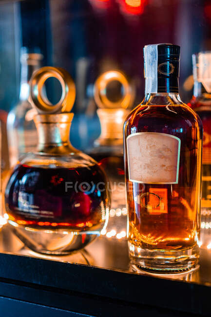 Bouteilles en verre transparent avec whisky placé sur le comptoir dans un bar sombre la nuit — Photo de stock