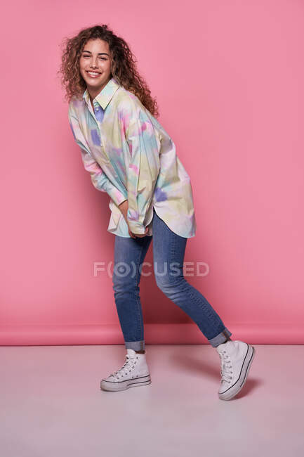 Positivo jovem mulher vestindo camisa de verão e jeans de pé sorrindo olhando para a câmera contra fundo rosa — Fotografia de Stock