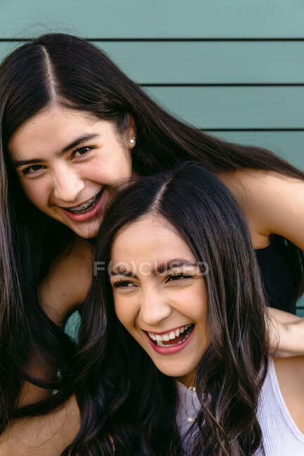 Aufrichtiger weiblicher Teenager lehnt mit den Händen auf dem Kopf von Geschwistern, während er tagsüber wegschaut — Stockfoto