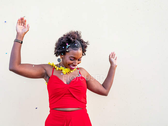 Excited African American female with arms outstretched and mouth opened standing under falling confetti at event against white background — Stock Photo