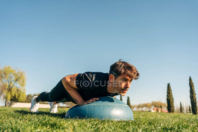 Ground level of determined male athlete in sportswear training on meadow while looking forward under blue sky — Stock Photo