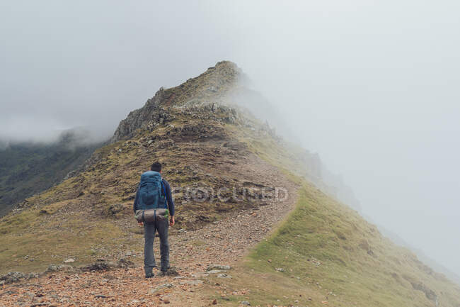 Back view of faceless male hiker walking along trail in highlands during trekking on foggy day in Wales — Stock Photo