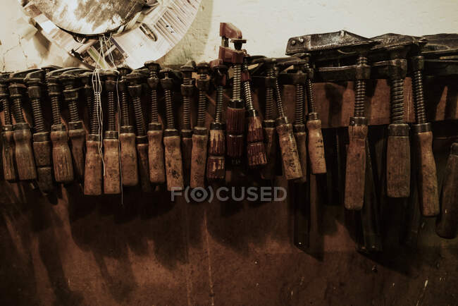 Set alter verwitterter Schraubgewindeklemmen in verschiedenen Formen, die in der alternden Geigenbauerwerkstatt an der Wand hängen — Stockfoto