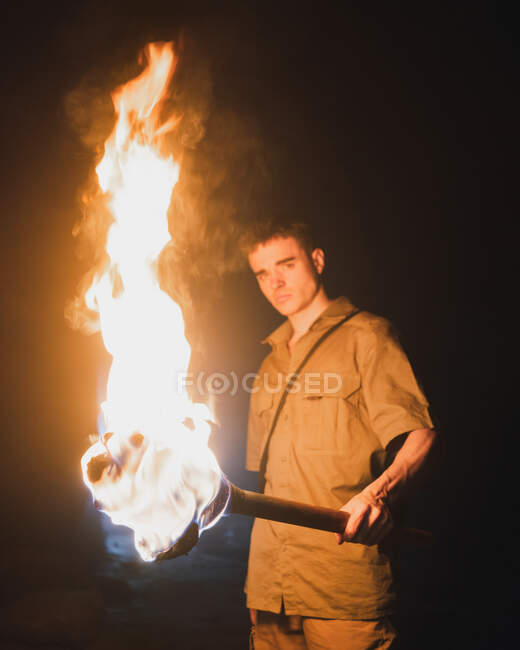 Side view of young male speleologist with flaming torch standing in dark narrow rocky cave while exploring subterranean environment — Stock Photo