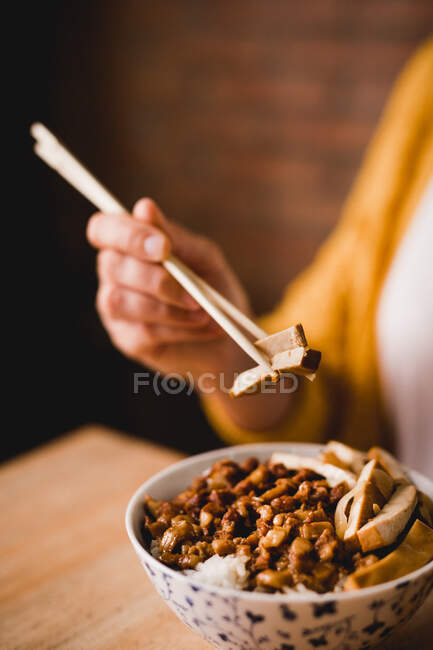 Руки жінки їдять з паличками з керамічної миски смачної страви Лу Ру Фан з тофу, розміщеної на столі в кафе — стокове фото