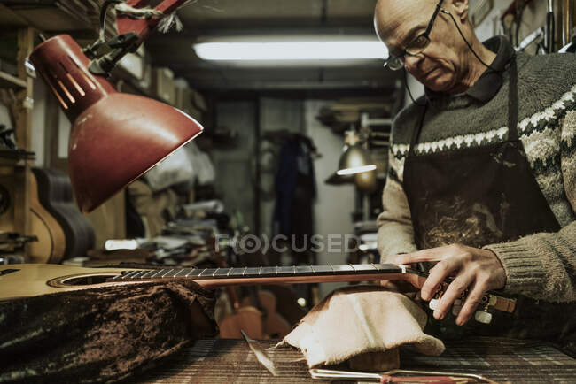 Maduro macho luthier em suéter medindo porca traste durante a reparação de guitarra acústica na oficina — Fotografia de Stock