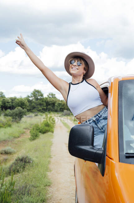 Viajante feminino alegre espreitando pela janela da van e mostrando gesto de dois dedos enquanto desfruta de viagem de carro no verão — Fotografia de Stock