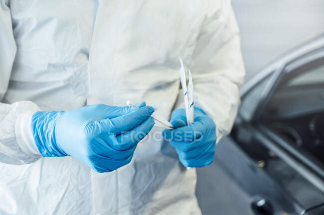 Biologiste avec des gants de protection effectuant un test de coronavirus sur une personne dans une voiture — Photo de stock