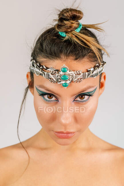 Beautiful young female model with oriental style makeup and stylish silver adornment with green gemstones on head — Stock Photo