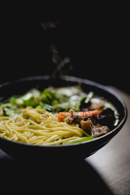 Schüssel mit herzhafter asiatischer Suppe mit Nudeln vor dunklem Hintergrund im Café — Stockfoto