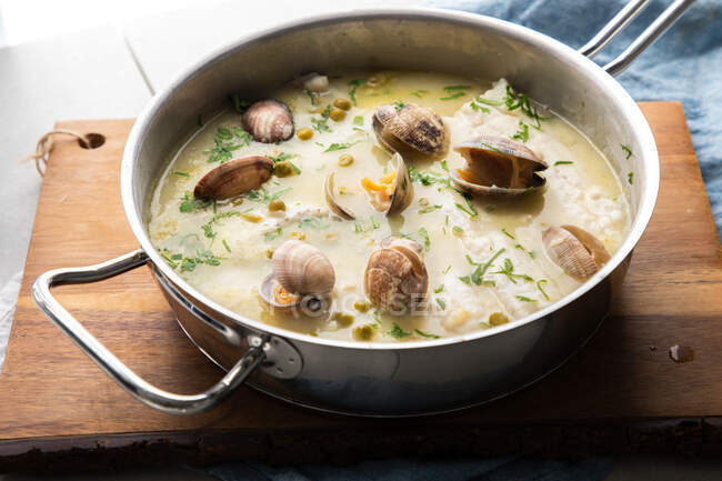 From above metal saucepan with delicious seafood soup with clams and hake placed on wooden board in kitchen — Stock Photo