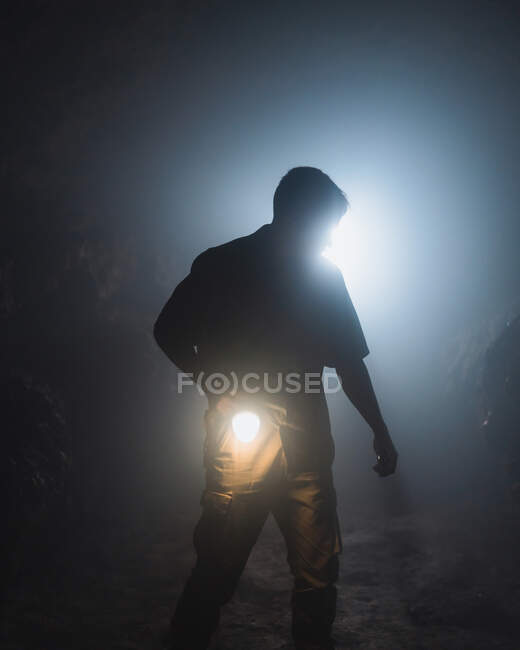 Unrecognizable male speleologist with bright flashlight in hand exploring dark subterranean cave during extremal adventure — Stock Photo