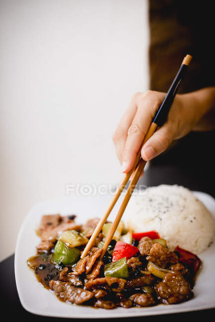 Рука анонімної жінки, використовуючи палички, щоб вибрати шматочок яловичини в смачному устричному соусі з тарілки в ресторані — стокове фото