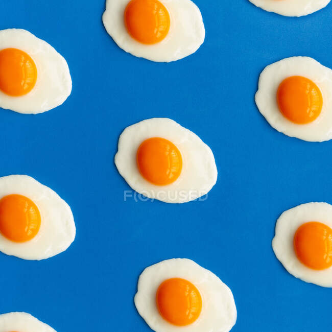 Fila de huevos fritos sobre un fondo azul - foto de stock