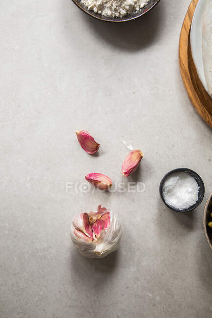 Сверху видна гвоздика спелого чеснока и маленькая миска соли, помещенная на кухонный стол во время приготовления пищи. — стоковое фото