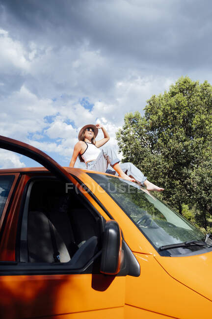 Baixo ângulo de sereno explorador do sexo feminino sentado no telhado da van e desfrutar de aventura de verão no dia ensolarado — Fotografia de Stock