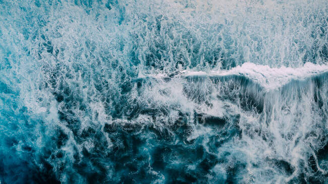 Drone view of abstract background of foamy sea waves of turquoise color rolling over seashore — Stock Photo