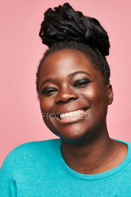 Mulher afro-americana feliz em roupas azuis olhando para a câmera de pé contra o fundo rosa — Fotografia de Stock