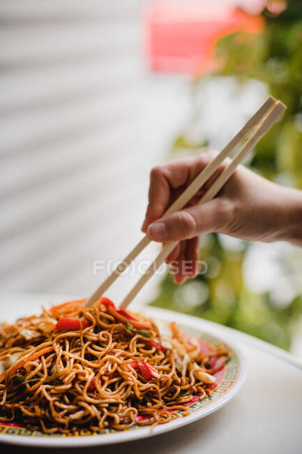 Hand eating fried tasty appetizing noodles with healthy vegetables with chopsticks in Asian cafe — Stock Photo