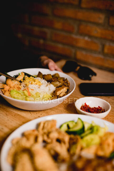 Woman in casual clothes with smartphone and sunglasses eating tasty Taiwanese bento with chopsticks in Asian cafe — Stock Photo