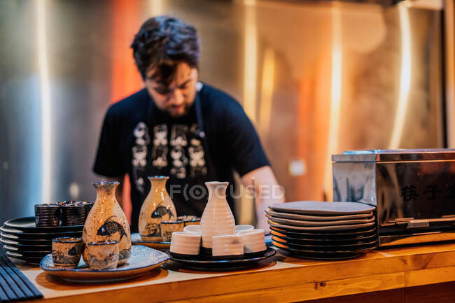Junger Mann in Schürze kocht asiatische Gerichte, während er in der Ramen-Bar am Tresen steht — Stockfoto