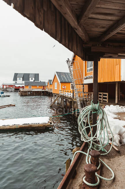 Molo di legno con galleggiante legato situato vicino a cabine gialle nella giornata invernale in insediamento costiero sulle isole Lofoten, Norvegia — Foto stock