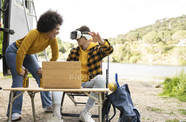 Cheerful man in VR glasses exploring virtual reality near delighted black girlfriend while resting in nature together — Stock Photo