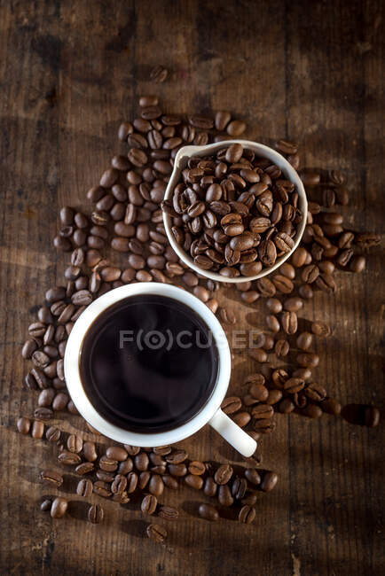 Vista superior do americano aromático quente na xícara colocada na mesa de madeira com grãos de café espalhados — Fotografia de Stock