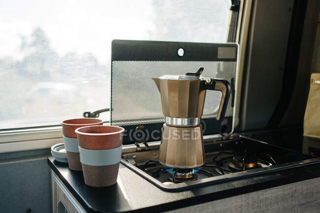 Coffee warming up in the kitchen of a motorhome next to two cups — Stock Photo