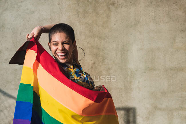 Zufriedene junge bisexuelle ethnische Frau mit bunter Flagge, die LGBTQ-Symbole darstellt und auf einen sonnigen Tag herabblickt — Stockfoto