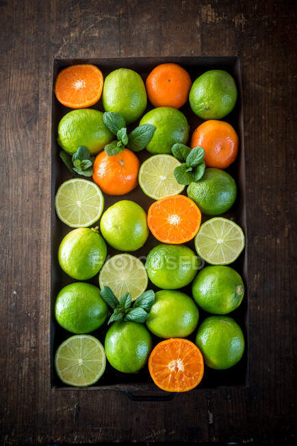 De cima de limas verdes maduras e laranjas colocadas na caixa na mesa rústica de madeira — Fotografia de Stock