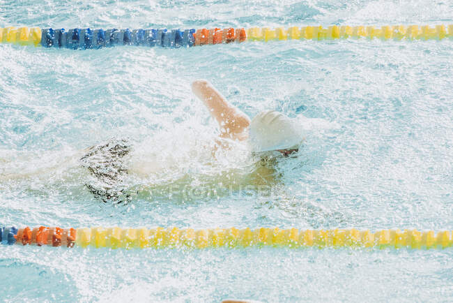 Vista laterale dello sportivo paralimpico in maschera e berretto senza nuoto a mano stile crawl in piscina tra le corsie — Foto stock
