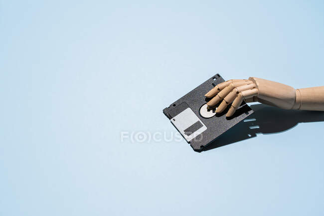 Haut angle de main en bois avec disquette rétro noire placée sur fond bleu clair — Photo de stock