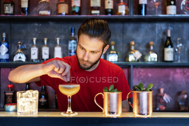 Focused barman decorating cocktail with green leaf served in glass goblet on counter in bar — Stock Photo