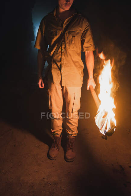 Обрізаний анонімний чоловічий спелеолог з палаючим факелом, що стоїть у темній вузькій скелястій печері, досліджуючи підземне середовище — стокове фото