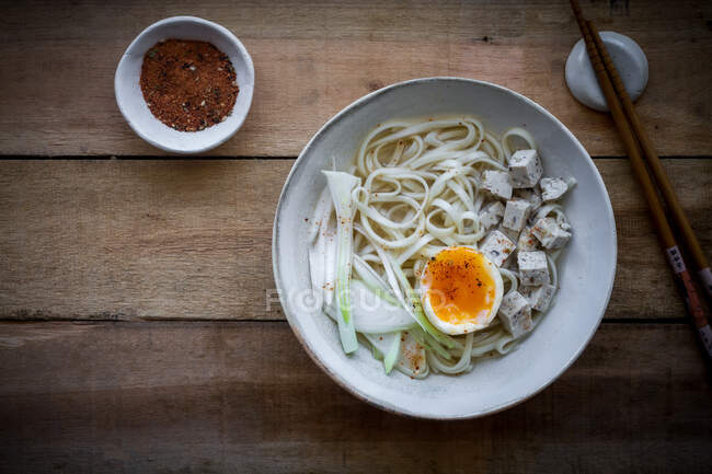 Nouilles ramen fraîches et cuites avec tofu, œufs et légumes servis sur un bol en céramique sur une table en bois — Photo de stock