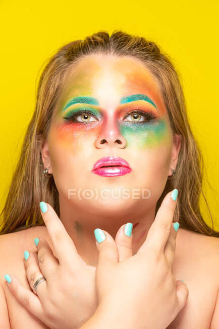 Плюс размер женщины с ярким цветным макияжем, отводящим взгляд на желтом фоне — стоковое фото