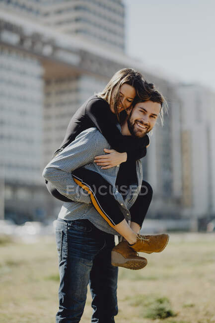 Uomo barbuto abbracciare donna mentre trascorre del tempo sul prato verde sulla strada insieme — Foto stock