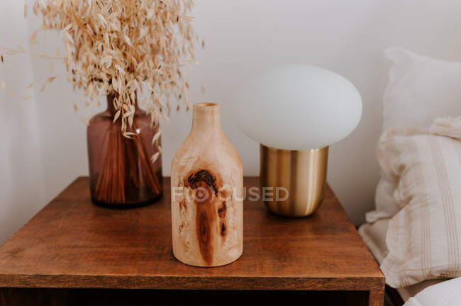 Vaso de madeira criativo colocado na mesa de cabeceira com lâmpada e plantas secas no quarto acolhedor — Fotografia de Stock
