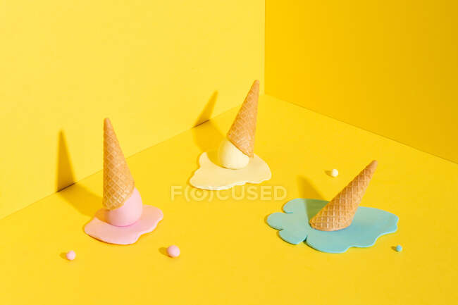 Mockup blau, gelb und rosa schmelzendes Eis in Waffelkegel auf gelbem Hintergrund, der das Sommerkonzept repräsentiert — Stockfoto
