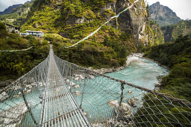 Metal suspension bridge crossing blue river in Himalayas mountains on sunny day in Nepal — Stock Photo