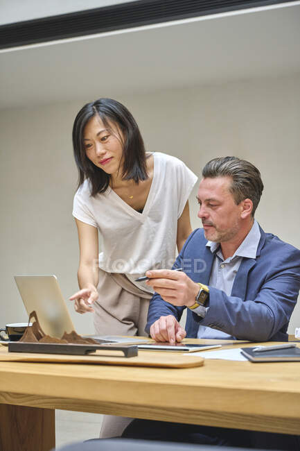 Diseñador en su escritorio trabajando en su computadora con su asistente - foto de stock
