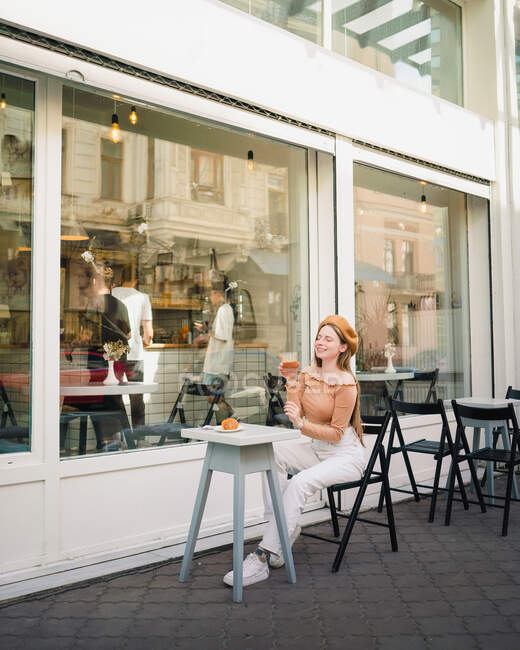 Femme française en béret assise à table dans un café avec verre de café aromatique et croissant fraîchement cuit — Photo de stock