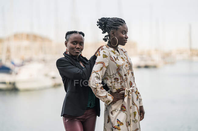 Conteúdo senhoras afro-americanas elegantes que ficam perto e olham para a câmera pensativa no parque em um dia brilhante — Fotografia de Stock