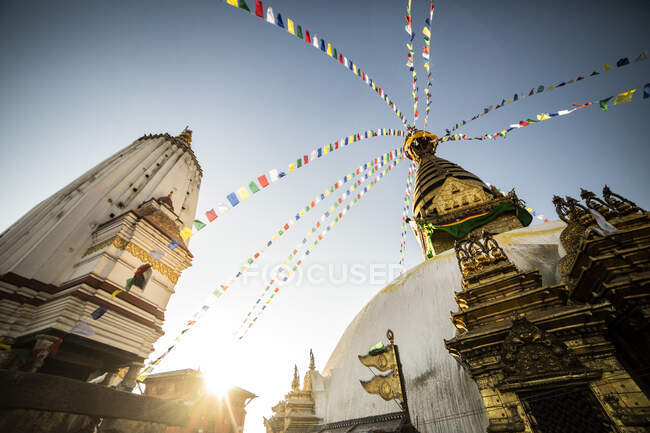 Bajo ángulo de Swayambhunath Stupa con guirnalda de bandera de oración en el antiguo complejo budista en el día soleado en Nepal - foto de stock